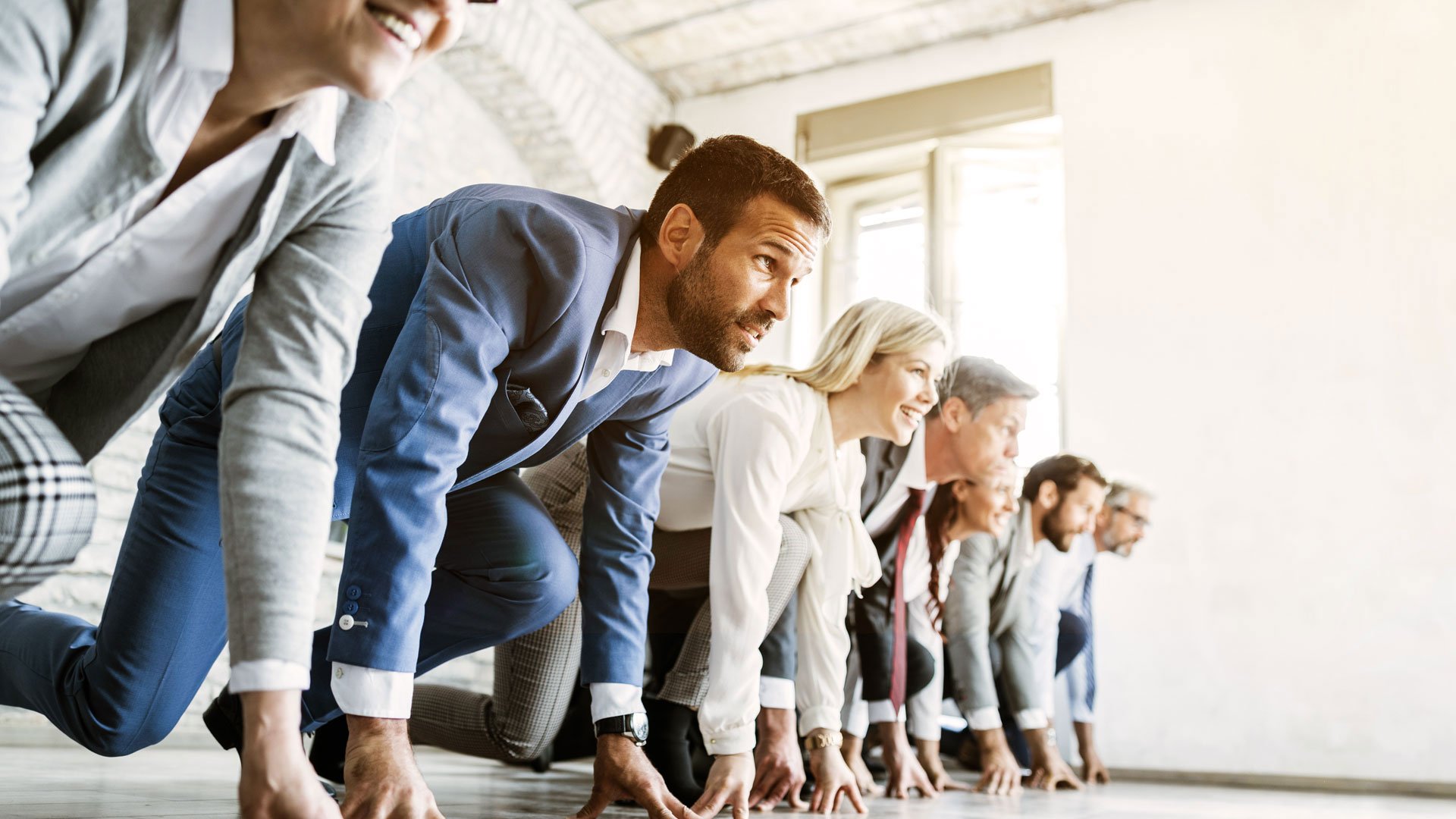 Mehrere Menschen in Businesskleidung stehen in Startposition wie bei einem Sprint.
