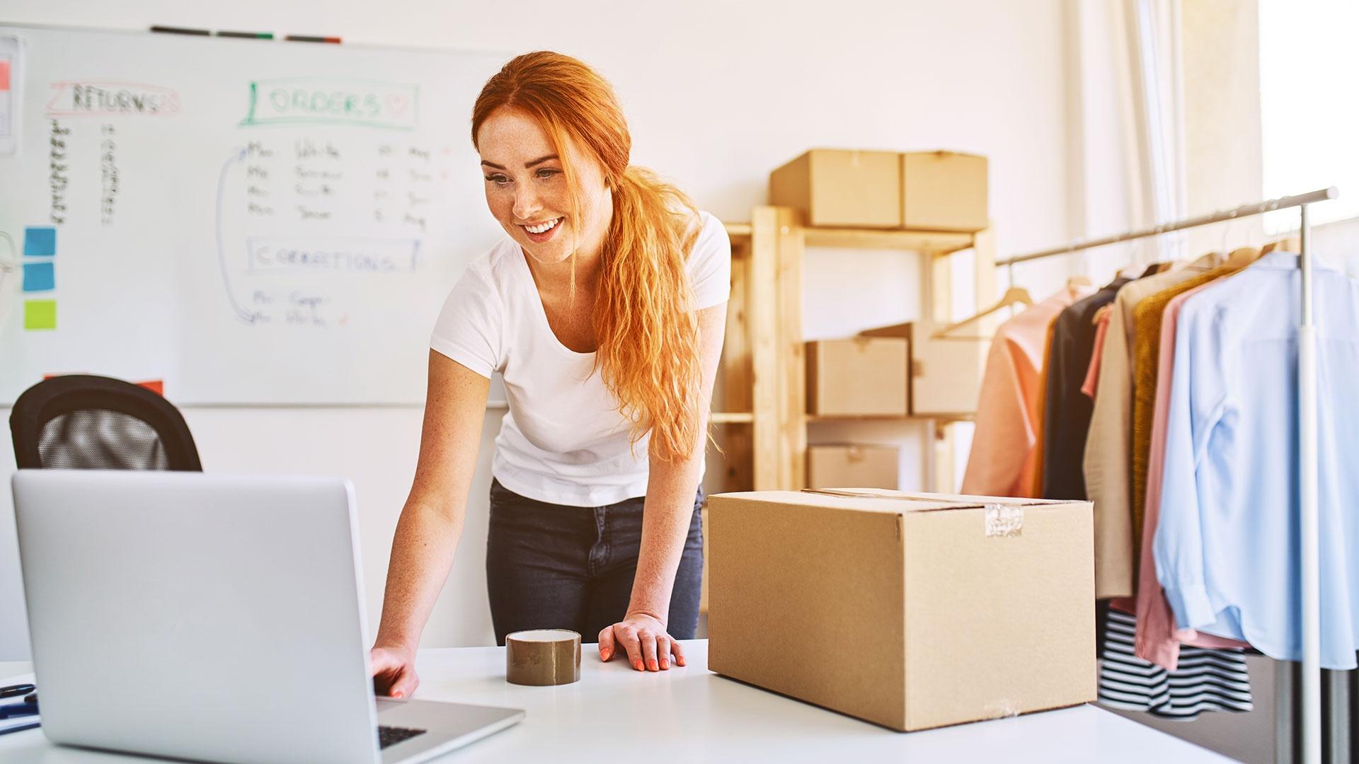Frau arbeitet als Selbstständige an Laptop und bereitet Paketversand vor – modernes Arbeiten mit Glasfaser-Internet.