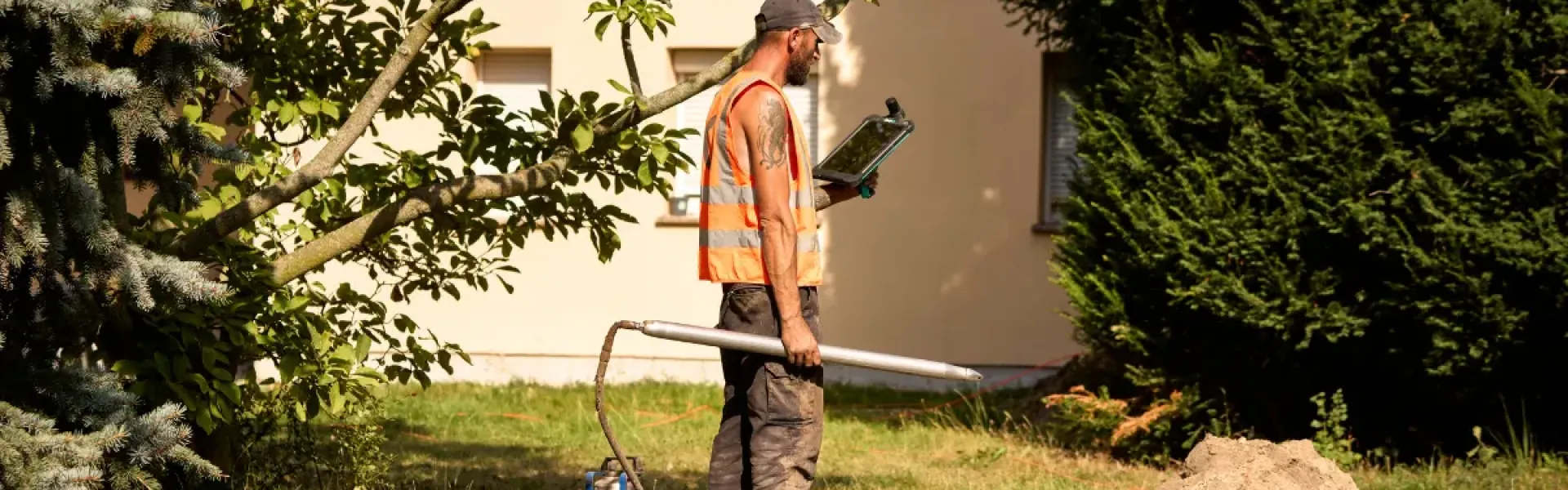 Bauarbeiter, der mit einem Tablet und einer Erdrakete im Garten steht