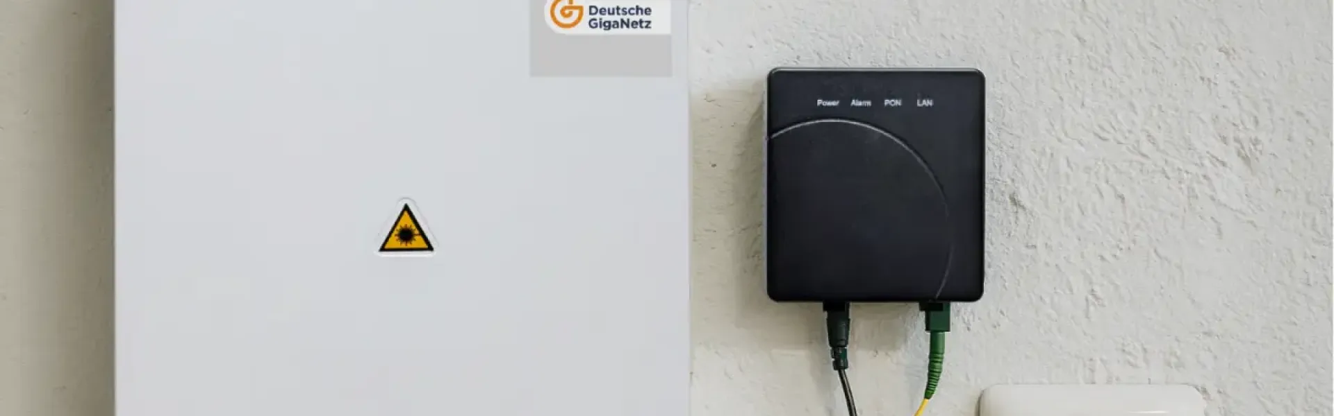 Glasfaser-Hausanschlusskasten mit verbundenem Netzabschlussgerät und Steckdose an der Wand.