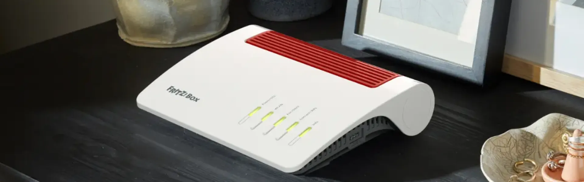 Router mit leuchtenden Statusanzeigen auf einem Regal neben Dekoobjekten.